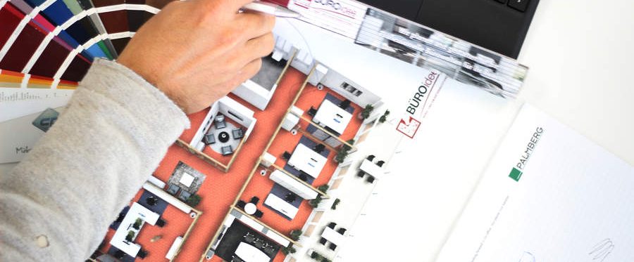 Hand mit Stift zeigt auf einen farbigen Büro-Grundriss, daneben ein Farbfächer